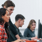 Four individuals working at computers in a classroom.