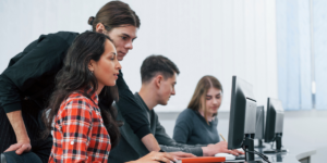 Four individuals working at computers in a classroom.