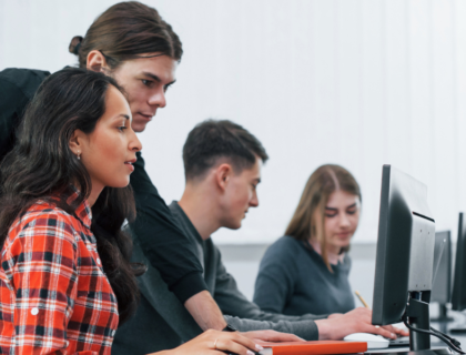 Four individuals working at computers in a classroom.