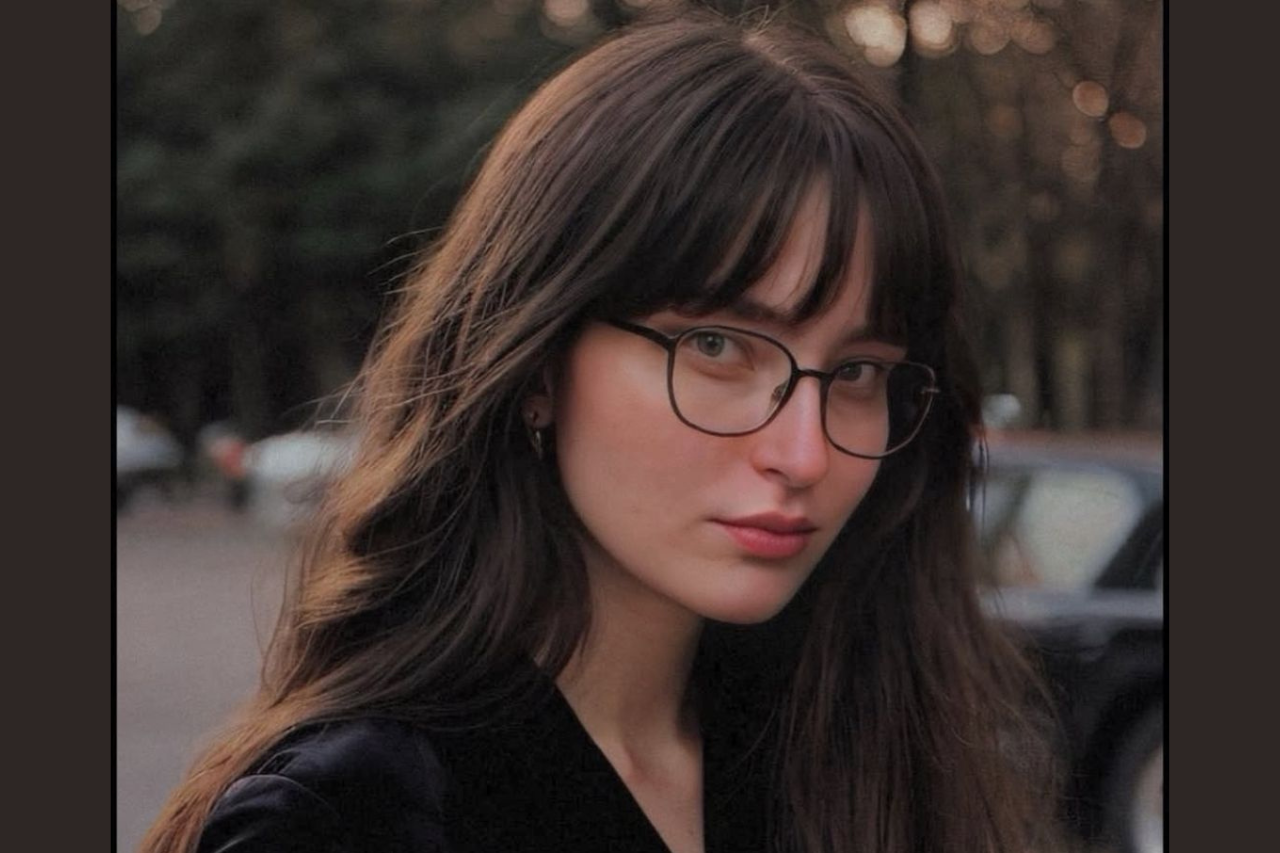 A woman wearing glasses and a black top, looking confidently at the camera.