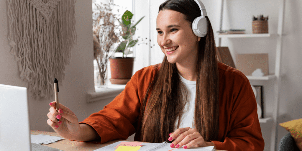 A woman wearing headphones sits at a desk, focused on her laptop while working or studying.