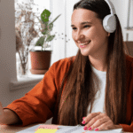 A woman wearing headphones sits at a desk, focused on her laptop while working or studying.