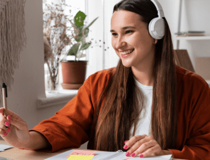A woman wearing headphones sits at a desk, focused on her laptop while working or studying.