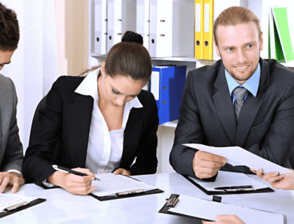 A group of business professionals seated at a table, reviewing documents and discussing strategies.