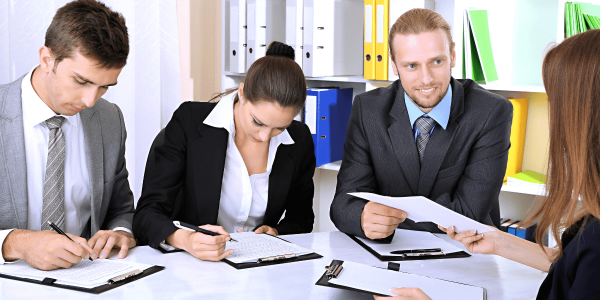 A group of business professionals seated at a table, reviewing documents and discussing strategies.