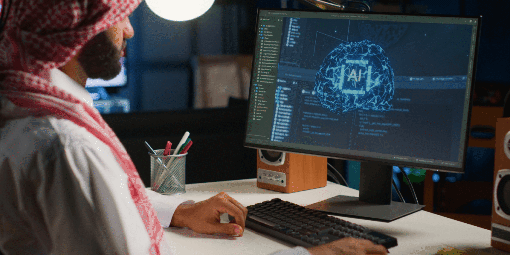 A man wearing a headscarf is focused on working at his computer.