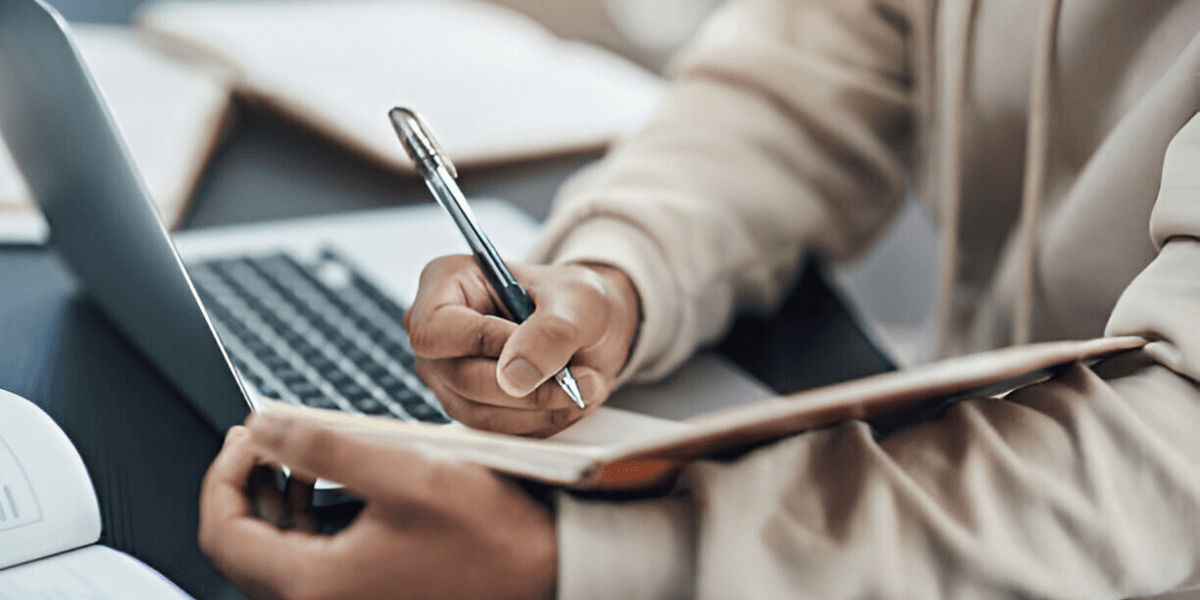 Benefits of Professional Training for Working Adults A man writes in a notebook with a pen while a laptop is open beside him on a desk.