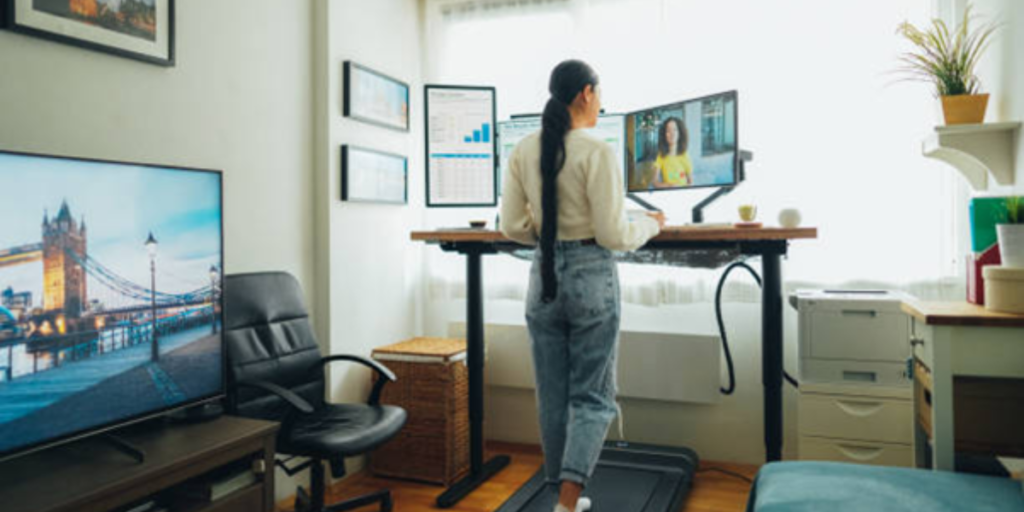 A woman stands on a treadmill, typing on a laptop while exercising.