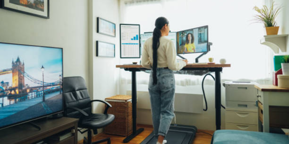 A woman stands on a treadmill, typing on a laptop while exercising.