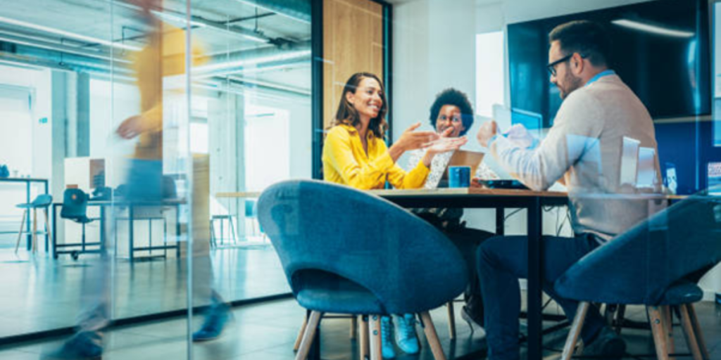 A group of diverse individuals seated around a table in a modern office setting, engaged in discussion.