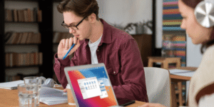 A man and woman sit at a table, each using a laptop, engaged in a collaborative work session.