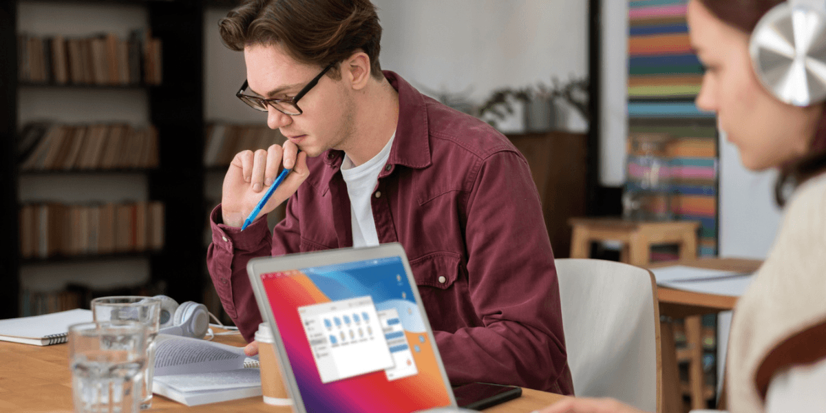A man and woman sit at a table, each using a laptop, engaged in a collaborative work session.