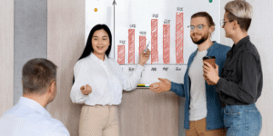 A group of five individuals discussing a chart displayed on a whiteboard in a collaborative setting.
